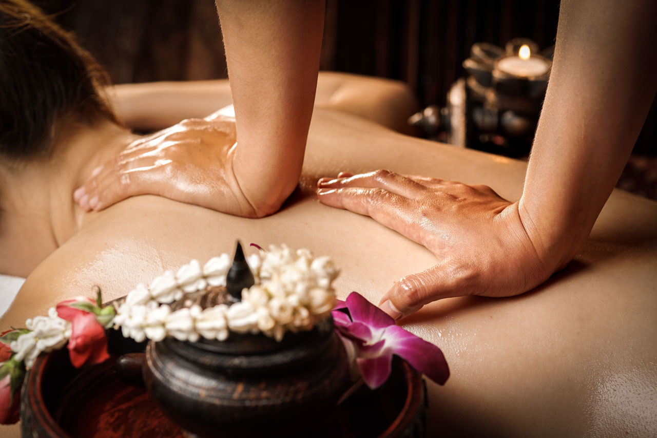 Two oil covered hands pressed firmly onto the middle of a persons back performing a massage